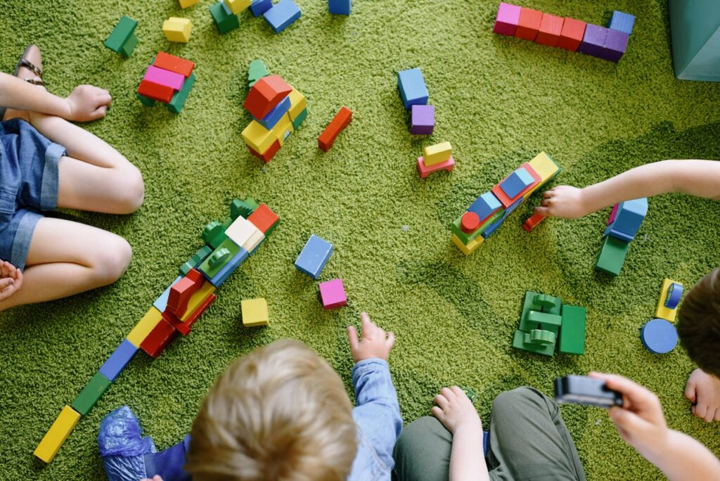 pexels photo 8535193 Children playing with wooden blocks on a green carpet in a classroom setting.